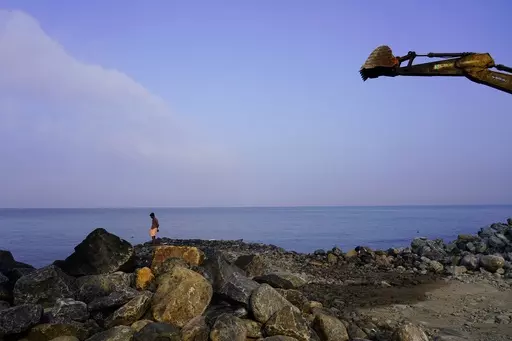 A man stands on the shore of the Arabian Sea near a digger that's part of a construction site for a new sea wall in the Chellanam area of Kochi, Kerala state, India on March 3, 2023. Tens of millions of people in India live along coastlines and thus are exposed to major weather events. (AP Photo)