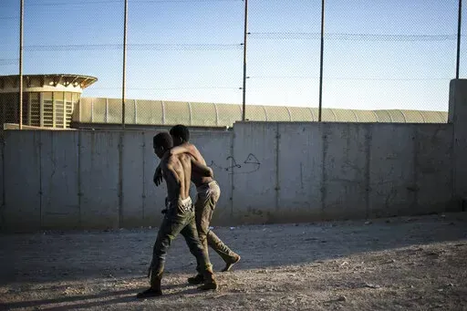 A migrant helps another as they arrive on Spanish soil after crossing the fences separating the Spanish enclave of Melilla from Morocco, in Melilla, Spain, Thursday March 3, 2022. Hundreds of Africans have tried to climb over the fences separating the Spanish city of Melilla from Morocco for the second consecutive day and the Spanish government's delegation in Melilla says that 380 of 1,200 migrants who had attempted to cross managed to overcome the double 6-meter (20-feet) barrier that perimete