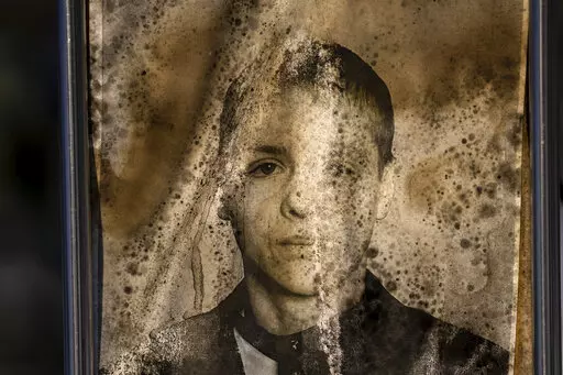 A worn-out portrait of Dmytro Andriyovych, 34, sits on his grave at a cemetery in Irpin, Ukraine, on the outskirts of Kyiv, on Friday, Feb. 10, 2023. He was buried on April 26, 2022. Exposed to rain, sun and frost over the course of a war that began nearly a year ago, the graveside portraits' once bright hues are fading away and yellow stains and mold are encroaching. (AP Photo/Emilio Morenatti)