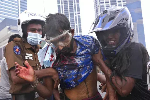 A Sri Lankan policeman, left, and a civilian helps an anti-government protester who was beaten up by government supporters during a clash in Colombo, Sri Lanka, Monday, May 9, 2022. Government supporters on Monday attacked protesters who have been camped outside the offices of Sri Lanka's president and prime minster, as trade unions began a “Week of Protests” demanding the government change and its president to step down over the country’s worst economic crisis in memory. (AP Photo/Eranga 