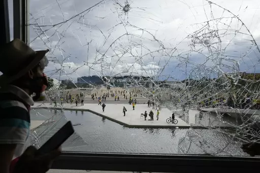 A protester, supporter of Brazil's former President Jair Bolsonaro, looks out from a shattered window of the Planalto Palace after he and many others stormed it, in Brasilia, Brazil, Jan. 8, 2023. Members of the three branches of power in Brazil say the country’s democracy and its guardrails have been restored after the trashing of the government buildings a year ago. But arrests have led supporters of the former president to say their freedom of speech is being violated and claim they are pol
