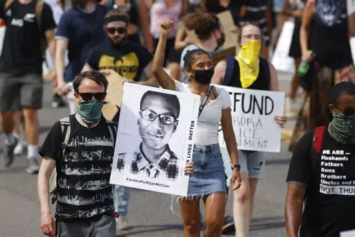 Demonstrators carry placards as they walk down Sable Boulevard during a rally and march over the death of Elijah McClain in Aurora, Colo., on June 27, 2020. A group of police officers and paramedics charged in the death of McClain, a 23-year-old Black man who was forcibly restrained and injected with a powerful sedative, are scheduled to appear in court Friday, Jan. 20, 2023, to enter pleas to the allegations. (AP Photo/David Zalubowski, File)