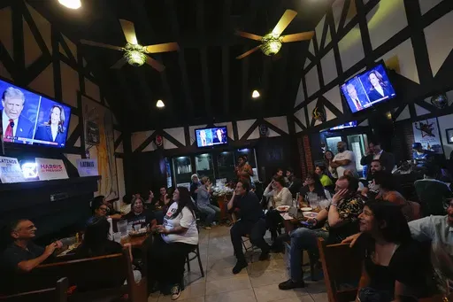 People watch TV screens showing a debate between Democratic presidential nominee Vice President Kamala Harris, right on screen, and Republican presidential nominee former President Donald Trump, at Sports Grill Kendall, where the Miami-Dade Democratic Hispanic Caucus had organized a watch party, Tuesday, Sept. 10, 2024, in Miami. (AP Photo/Rebecca Blackwell, File)