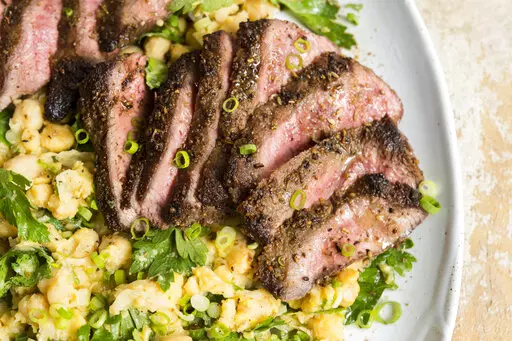 This image released by Milk Street shows a recipe for Spice-Crusted Steak with a side of partially mashed chickpeas. (Milk Street via AP)