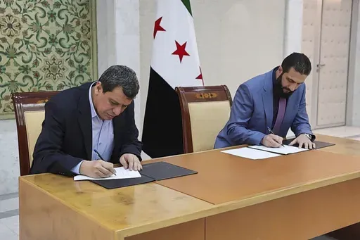In this photo released by Syrian state news agency SANA, Syria's interim President Ahmad al-Sharaa, right, and Mazloum Abdi, the commander of the U.S.-backed Kurdish-led Syrian Democratic Forces, sign a deal in Damascus, Syria, Monday, March 10, 2025. (SANA via AP)
