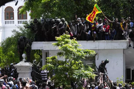 Protesters, one carrying national flag, storm the Sri Lankan Prime Minister Ranil Wickremesinghe's office, demanding he resign after president Gotabaya Rajapaksa fled the country amid economic crisis in Colombo, Sri Lanka, Wednesday, July 13, 2022. Rajapaksa fled on a military jet on Wednesday after angry protesters seized his home and office, and appointed Prime Minister Ranil Wickremesinghe as acting president while he is overseas. Wickremesinghe quickly declared a nationwide state of emergenc