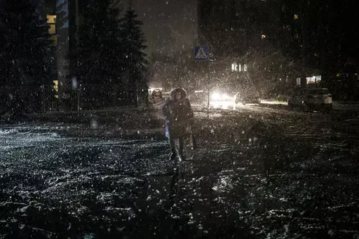 A woman crosses the street during snowfall, as power outages continue in Kyiv, Ukraine, Friday, Dec. 16, 2022. Russia's repeated attacks on Ukraine's energy infrastructure have left millions of civilians in the cold and the dark as temperatures plummet. (AP Photo/Felipe Dana, File)