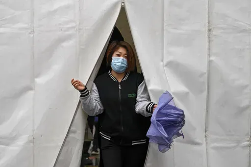 A woman wearing a face mask to help protect from the coronavirus walks out from a tent after getting a COVID-19 test, Tuesday, March 29, 2022, in Beijing. A two-phase lockdown of Shanghai's 26 million people is testing the limits of China's hard-line "zero-COVID" strategy, which is shaking markets far beyond the country's borders. (AP Photo/Andy Wong)