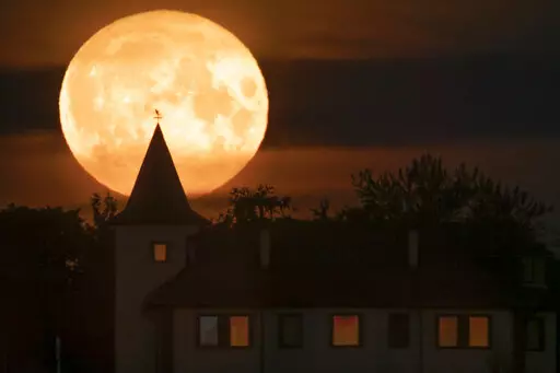 The full moon rises over a private house in the village of Putilovo, 70 kilometeres (43 miles) east of St. Petersburg, Russia, late Wednesday, July 13, 2022. (AP Photo/Dmitri Lovetsky)