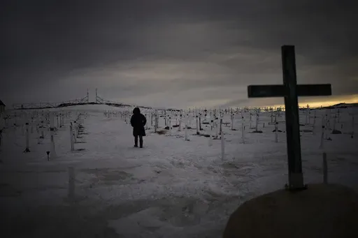 A woman walks at a graveyard covered by snow as the sun sets in Nuuk, Greenland, Sunday, Feb. 16, 2025. (AP Photo/Emilio Morenatti)