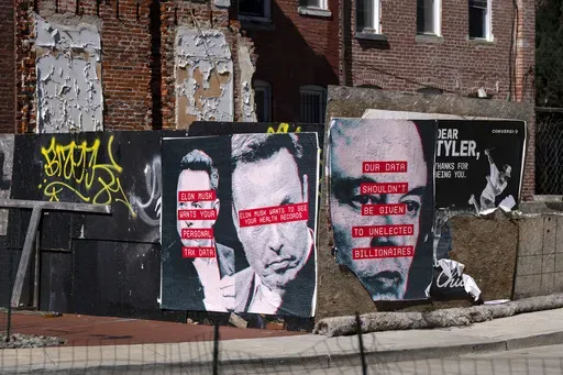 Posters showing the face of Elon Musk and messages relating to data privacy are seen on a fence surrounding a building site in Washington, Friday, March 7, 2025. (AP Photo/Ben Curtis)