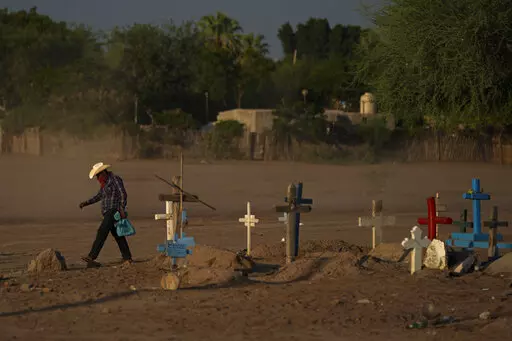 A Yaqui Indigenous wears a bandana over his mouth as he walks through dust past the cemetery where slain water-defense leader Tomás Rojo is buried in Potam, Mexico, Tuesday, Sept. 27, 2022. Rojo was a descendent of Tetabiate, a Yaqui leader killed in a 1901 battle with the government, which deported the surviving Yaquis to work in slave-like conditions on henequen plantations in far-away Yucatan. (AP Photo/Fernando Llano)