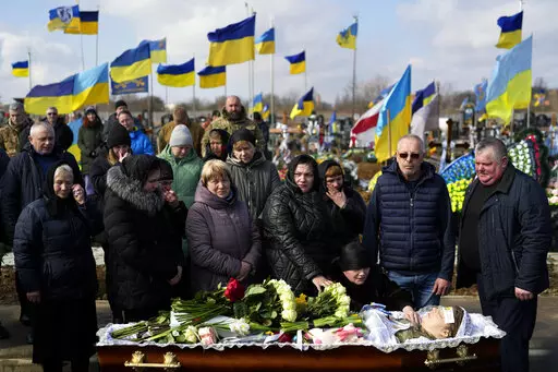 Relatives gather next to the body of 29 year old Yana Rikhlitska, a Ukrainian army medic killed in the Bakhmut area, during the funeral in Vinnytsia, Ukraine, Tuesday, March 7, 2023. Just over a week ago, Yana Rikhlitska was filmed by The Associated Press as she helped treat wounded soldiers in a field hospital of Bakhmut area which has been pulverized as Russia presses a three-sided assault to seize it. (AP Photo/Thibault Camus)