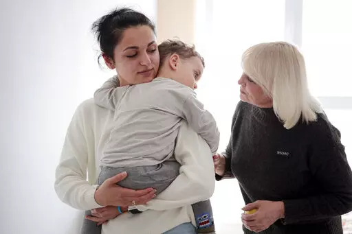Karina Buiukli, 27-years-old, holds her 2-year-old son, Maxim as her mother Galina Stepanova, right, watches after an interview with The Associated Press, in Brasov, Romania, Wednesday, March 30, 2022. Having escaped from Russian shelling, Ukrainian refugees are now focused on building new lives — temporarily or permanently. Countries neighboring their homeland, like Poland and Romania, are sparing no effort to help them integrate and feel needed in the new environment.(AP Photo/Stephen McGrat