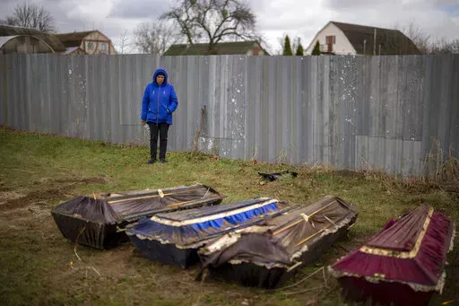 CAPTION CORRECTS LOCATION - Ira Slepchenko, 54, stands next to coffins, one of them with the body of her husband Sasha Nedolezhko, 43, during an exhumation of a mass grave in Mykulychi, Ukraine on Sunday, April 17, 2022. All four bodies in the village grave were killed on the same street, on the same day. Their temporary caskets were together in a grave. On Sunday, two weeks after the soldiers disappeared, volunteers dug them up one by one to be taken to a morgue for investigation. (AP Photo/Emi