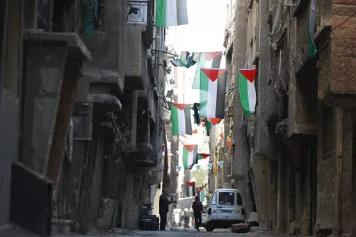 People walk under Palestinian flags in Yarmouk camp in Damascus Syria that has seen heavy fighting during the civil war, Wednesday, Nov. 2, 2022. A trickle of residents has returned to Yarmouk, the large Palestinian refugee camp-turned-Damascus neighborhood that was devastated in the country's civil war. (AP Photo/Omar Sanadiki, File)