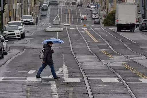 A pedestrian carries an umbrella while crossing a street in San Francisco, Thursday, April 14, 2022. A variety of new laws take effect Sunday, Jan. 1, 2023 that could have an impact on people's finances and, in some cases, their personal liberties. (AP Photo/Jeff Chiu, File)
