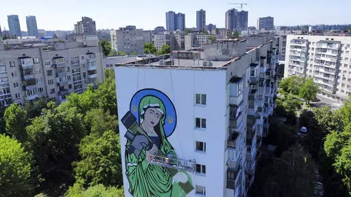 A worker paints a "Saint Javelin", a Virgin Mary holding an American-made anti-tank missile, in Kyiv, Ukraine, Tuesday, May 24, 2022. No matter where they live, the 3-month-old war never seems to be far away for Ukrainians. Those in towns and villages near the front lines hide in basements from constant shelling, struggling to survive with no electricity or gas — and often no running water. But even in regions out of the range of the heavy guns, frequent air raid sirens wail as a constant remi