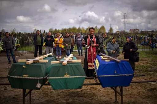 A priest blesses the remains of three people who died during the Russian occupation and were disinterred from temporary burial sites in Bucha, on the outskirts of Kyiv, on Wednesday, April 27, 2022. (AP Photo/Emilio Morenatti)