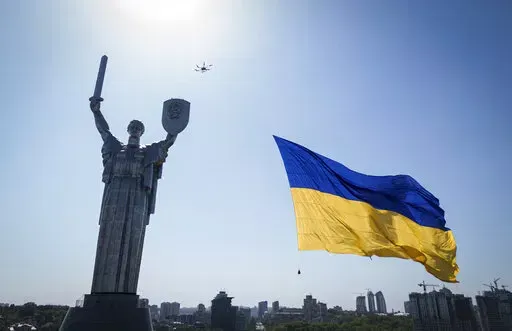A drone carries a big national flag in front of Ukraine's the Motherland Monument in Kyiv, Ukraine, Wednesday, Aug. 24, 2022. Kyiv authorities have banned mass gatherings in the capital through Thursday for fear of Russian missile attacks. Independence Day, like the six-month mark in the war, falls on Wednesday. (AP Photo/Evgeniy Maloletka)