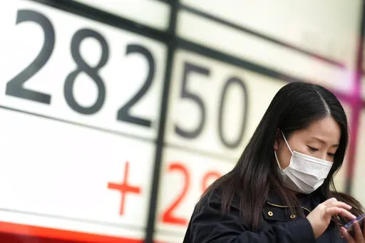 A woman uses her phone in front of monitors showing Japan's Nikkei 225 index at a securities firm while waiting for a traffic light in Tokyo, Thursday, Dec. 1, 2022. Shares have advanced in Asia after a rally on Wall Street spurred by the Federal Reserve chair's comments on easing the pace of interest rate hikes to tame inflation.(AP Photo/Hiro Komae)
