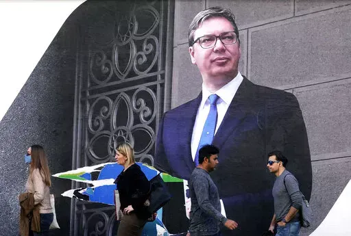 People walk by the pre-election billboard showing Current Serbian President and the Serbian Progressive Party leader Aleksandar Vucic in Belgrade, Serbia, Monday, March 28, 2022. Serbia's populist President Aleksandar Vucic, who has fostered close ties with Russia and refused to impose sanctions against Moscow over its invasion of Ukraine, is expected to extend his almost 10-year grip on power in the Balkan country at an election on Sunday. (AP Photo/Darko Vojinovic)