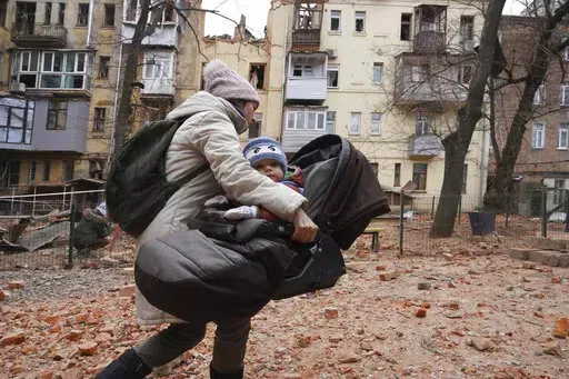 A woman carries her child as they evacuate from a residential building which was hit by a Russian rocket at the city center of Kharkiv, Ukraine, Monday, Jan. 30, 2023. Russian shelling killed at least five people and wounded 13 others during the previous 24 hours, Ukrainian authorities said Monday as the Kremlin’s and Kyiv’s forces remained locked in combat in eastern Ukraine. (AP Photo/Andrii Marienko)
