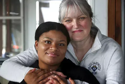 Deanna Cook, left, poses for a photograph with her mother Colleen at their home in Malden, Mass., Tuesday, March 15, 2022. A bill aimed at banning race-based discrimination targeting hair texture and hairstyles was unanimously approved Thursday, March 17, 2022 by the Massachusetts House. The issue came to light when the parents of then-15-year-old Black girls, Deanna and Mya Cook, said their twin daughters were punished for wearing extensions, while white students hadn't been punished for violat