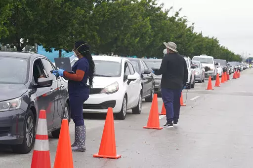 Employees of Nomi Health check in a long line of people for COVID-19 tests, Tuesday, Dec. 21, 2021, in North Miami, Fla. The omicron variant has unleashed a fresh round of fear and uncertainty, for travelers, shoppers and party-goers around the U.S. (AP Photo/Marta Lavandier)