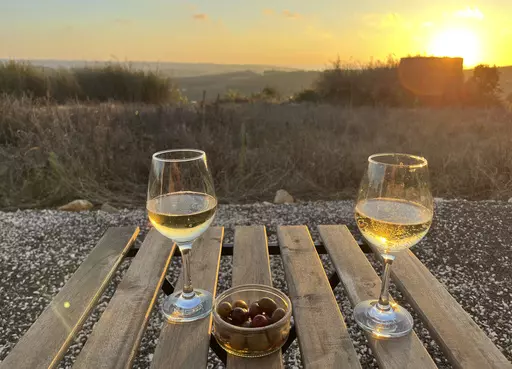 Glasses of Vinho Verde and local olives appear at sunset outside an old windmill-turned-Airbnb in the hills above Lourinhã, Portugal on Sept. 12, 2023, (Kristen de Groot via AP)