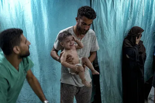 A Palestinian man holds a child wounded in the Israeli bombardment of the Gaza Strip in a hospital in Deir al-Balah, Thursday, July 18, 2024. (AP Photo/Abdel Kareem Hana)