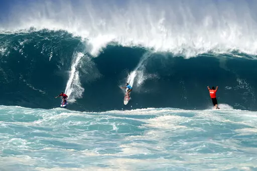 Kai Lenny, left, and Aaron Gold, center, are cheered on by Jake Maki, right, in Hawaii's Waimea Bay on Oahu’s North Shore during the The Eddie Aikau Big Wave Invitational surfing contest Sunday, Jan. 22, 2023. (Jamm Aquino/Honolulu Star-Advertiser via AP)