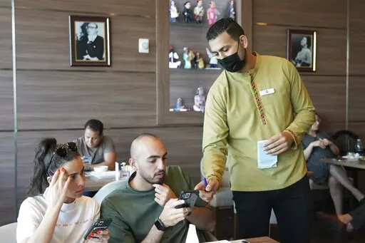 Ali el-Sayyed Mohammed takes an order from customers at Hadoota Masreya Restaurant in Dubai, United Arab Emirates, Sept. 5, 2022. Mohammed left his hometown of Beheira along the Egyptian Nile Delta this year to come to Dubai in the hopes of earning a living wage. The 26-year-old said he is supporting his mother and sisters back home and hoping to save enough to get married. (AP Photo/Malak Harb)