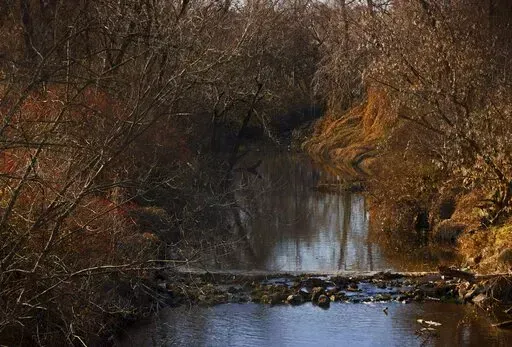 Water flows in Coldwater Creek on Thursday, Dec. 9, 2021, behind a row of homes at Belcroft Drive and Old Halls Ferry Road in Missouri's St. Louis County. Environmental investigation consultants have found significant radioactive contamination at an elementary school, which sits in the flood plain of Coldwater Creek which was contaminated by nuclear waste from weapons production during World War II. (Christian Gooden/St. Louis Post-Dispatch via AP)