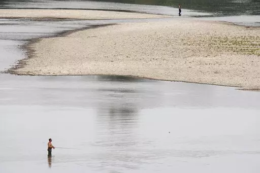People fish near a hydroelectric power plant at Isola Serafini, on the Po river in San Nazzaro, Italy, Wednesday, June 15, 2022. The drying up of the river is jeopardizing drinking water in Italy's densely populated and highly industrialized districts and threatening irrigation in the most intensively farmed part of the country.  (AP Photo/Luca Bruno)