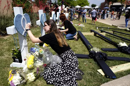 In this May 8, 2023, photo, Jennifer Seeley leaves a message on a cross that has the name of security guard Christian LaCour, written on it at a makeshift memorial in Allen, Texas. Jennifer Seeley was glued to her phone, safe at home but terrified nonetheless. There was an active shooter at the Texas mall where she works as an assistant store manager. And she was searching desperately for information, praying. Was the gunman dead? Were her coworkers dead? What was happening? (AP Photo/Tony Gutie