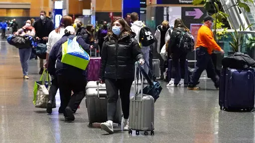 Travelers trek through Terminal E at Logan Airport, Tuesday, Dec. 21, 2021, in Boston.  At least three major airlines say they have canceled dozens of flights, Friday, Dec. 24,  because illnesses largely tied to the omicron variant of COVID-19 have taken a toll on flight crew numbers during the busy holiday travel season.  (AP Photo/Charles Krupa)