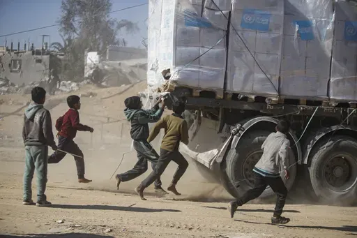 Palestinians chase humanitarian aid trucks that arrived through the Kerem Shalom crossing from Egypt into the Gaza Strip, in Rafah, Tuesday, Jan. 21, 2025. (AP Photo/Jehad Alshrafi)