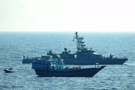 This photo released by the U.S. Navy, shows U.S. service members conduct a boarding on a stateless fishing vessel transiting international waters in the Gulf of Oman as a rigid-hull inflatable boat and patrol coastal ship USS Chinook (PC 9) sail nearby, Tuesday, Jan. 18, 2022. The U.S. Navy announced Sunday, Jan. 23 that it seized the boat in the Gulf of Oman carrying fertilizer used to make explosives that was caught last year smuggling weapons to Yemen. (U.S. Navy via AP)