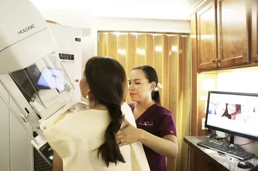 Mammographer Alma Garcia, right, demonstrates the process of a mammogram on marketing liaison Dalilah Garcia of the Neighbors Emergency Center in Brownsville, Texas, on Monday, Sep. 18, 2017, inside a Mammos on the Move (MOM) mobile mammogram trailer. According to a draft recommendation from a government task force released on Tuesday, May 9, 2023, women should start getting every-other-year mammograms at age 40 instead of waiting until 50. Tuesday’s update – if the draft proposal is finaliz