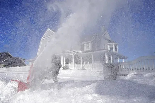 Bill McKelvey, of Scituate, Mass., uses a snow blower to clear snow in front of his home, Sunday, Jan. 30, 2022, in Scituate. (AP Photo/Steven Senne)