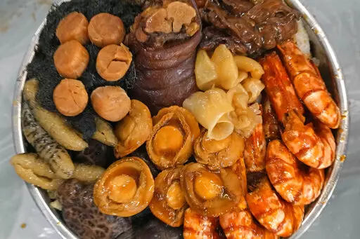 "Poon Choi" ingredients including chunks of seafood like abalone, sea cucumber, dried scallops, oysters and prawns together with pork knuckle and fragrant mushrooms, are seen in a basin at the RenRen Heping Restaurant in Hong Kong on Jan. 21, 2022. Tighter COVID-19 restrictions, including a ban on dining in restaurants after 6 p.m., are making Hong Kong residents plan their annual reunion dinner on Lunar New Year’s eve at home. (AP Photo/Kin Cheung)