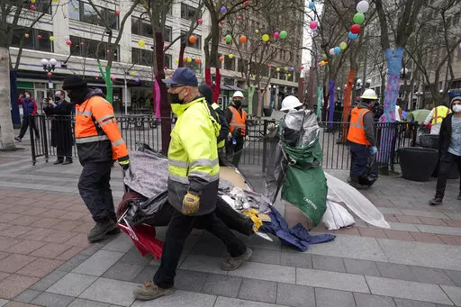 Workers carry a tent used by people experiencing homelessness to a garbage truck, Friday, March 11, 2022, during the clearing and removal of several tents at an encampment in Westlake Park in downtown Seattle. Increasingly in liberal cities across the country — where people living in tents in public spaces have long been tolerated — leaders are removing encampments and pushing other strict measures to address homelessness that would have been unheard of a few years ago. (AP Photo/Ted S. Warr