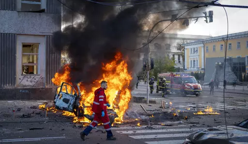 A medical worker runs past a burning car after a Russian attack in Kyiv, Ukraine, Monday, Oct. 10, 2022. The Russian missiles that rained down Monday on cities across Ukraine, bringing fear and destruction to areas that had seen months of relative calm, are an escalation in Moscow's war against its neighbor. But military analysts say it’s far from clear whether the strikes mark a turning point in a war that has killed thousands of Ukrainians and sent millions fleeing from their homes. (AP Phot