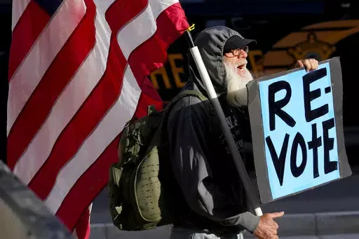 A man protests outside the Maricopa County Board of Supervisors auditorium prior to the board's general election canvass meeting, Nov. 28, 2022, in Phoenix. Worries that rogue county officials could undermine election results by refusing to certify them have lessened significantly in the wake of the midterms, with a lone Arizona county as the exception. Still, baseless attacks on the accuracy of the election by Republican county officials and angry members of the public already are raising conce