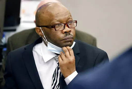 Defendant Billy Chemirmir lowers his mask as a state witness is asked to identify him during his murder trial at the Frank Crowley Courts Building in Dallas, Nov. 17, 2021. The retrial of the man charged with killing 18 older women in the Dallas area over a two-year span is set to begin Monday, April 25, 2022 after the first jury to hear a case against him deadlocked. Chemirmir faces life in prison without parole if he’s convicted of capital murder in the smothering of 81-year-old Lu Thi Harri