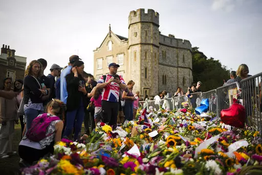 People gather at flowers and messages to tribute Queen Elizabeth II, in front of Windsor Castle in Windsor, England, Sunday, Sept. 11, 2022. Queen Elizabeth II, Britain's longest-reigning monarch and a rock of stability across much of a turbulent century, died Thursday Sept. 8, 2022, after 70 years on the throne. She was 96. (AP Photo/Markus Schreiber)