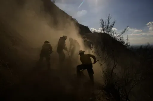 Members of the Navajo Scouts firefighter crew kick up dust as they clear debris from a landslide across a road on a hillside as they battle the Eaton Fire, Friday, Jan. 17, 2025, in Altadena, Calif. (AP Photo/John Locher)