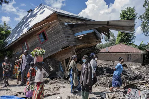 People walk next to a house destroyed by the floods in the village of Nyamukubi, South Kivu province, in Congo, Saturday, May 6, 2023. The death toll from flash floods and landslides in eastern Congo has risen according to the governor and authorities in the country's South Kivu province. (AP Photo/Moses Sawasawa)