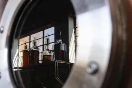 Bottles of The Bard product are seen in the reflection of a new column still that is not yet in use at The Bard Distillery in Graham, Ky., Sunday, March 9, 2025. (AP Photo/Jon Cherry)